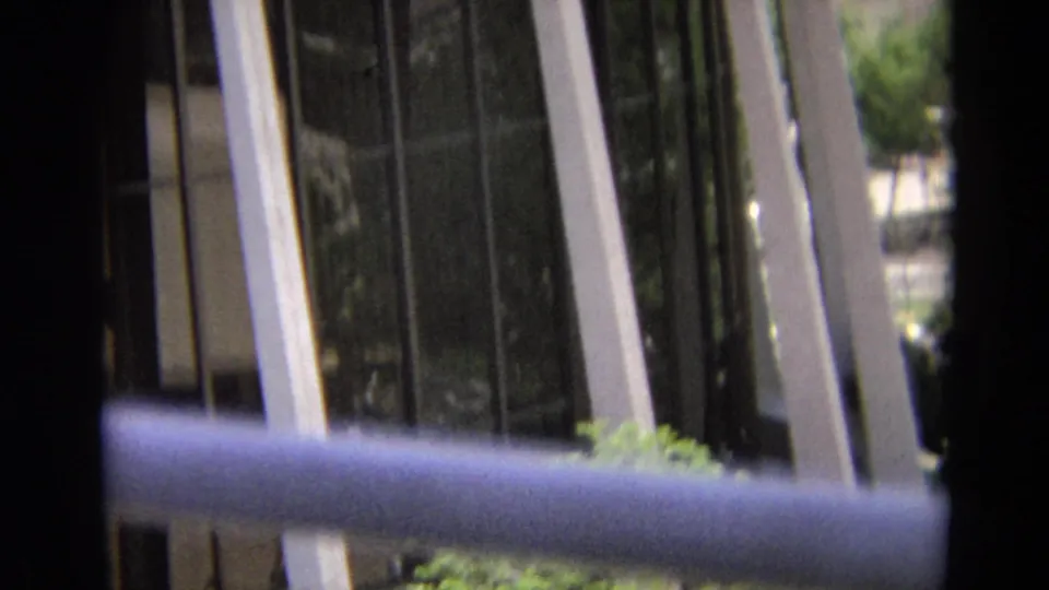 1968 Branson home-movie frame showing a glass-fronted building partly obscured by foreground bars and a rail.