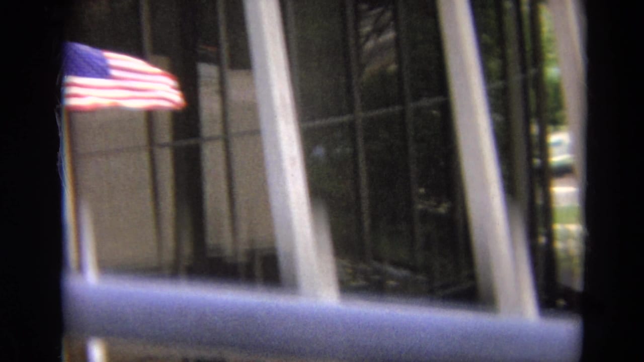 American flag waves outside a tall glass-fronted building in the 1968 Branson travel footage.