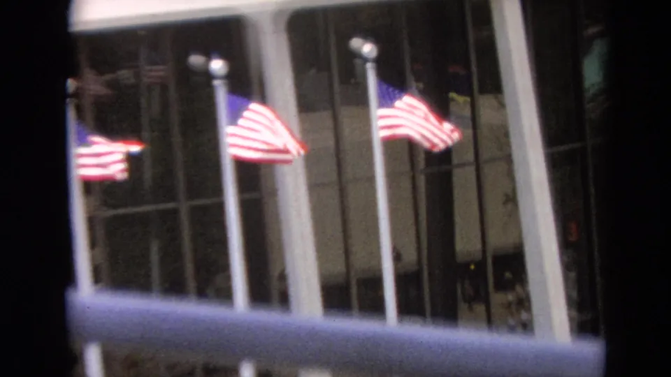 Three American flags stand before tall reflective windows in this Branson, Missouri home-movie frame.