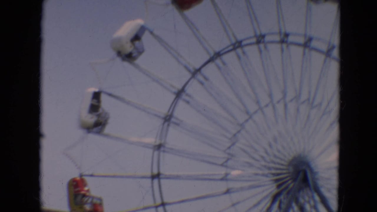 Large Ferris wheel against a pale sky with red and white passenger cars.