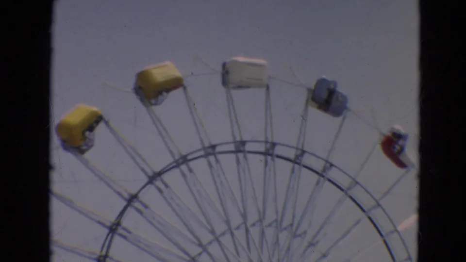 Branson 1968 carnival footage showing colorful Ferris wheel cars spaced along the wheel against a hazy sky.
