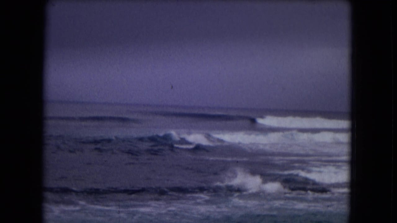 Rough ocean waves under a dark overcast sky with black 8mm frame borders.