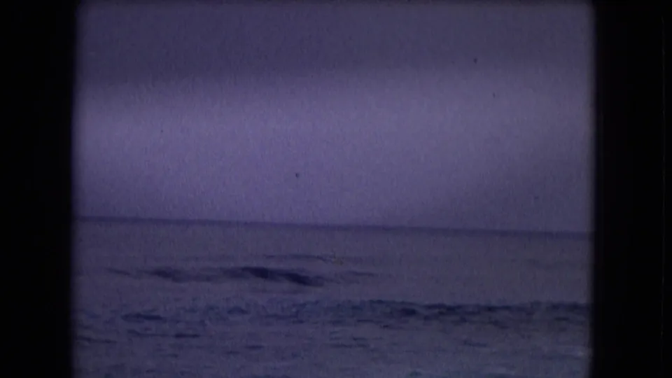 1968 Honolulu 8mm frame shows a subdued ocean horizon and choppy water under a purple-gray sky.