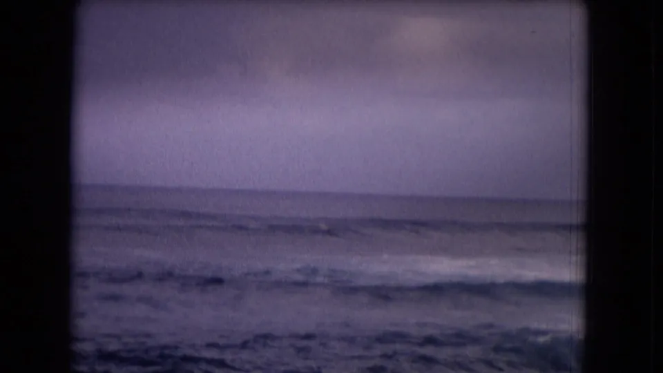 1968 Honolulu 8mm frame showing calm ocean swells beneath a hazy sky, with a distant surfer barely visible in the water.