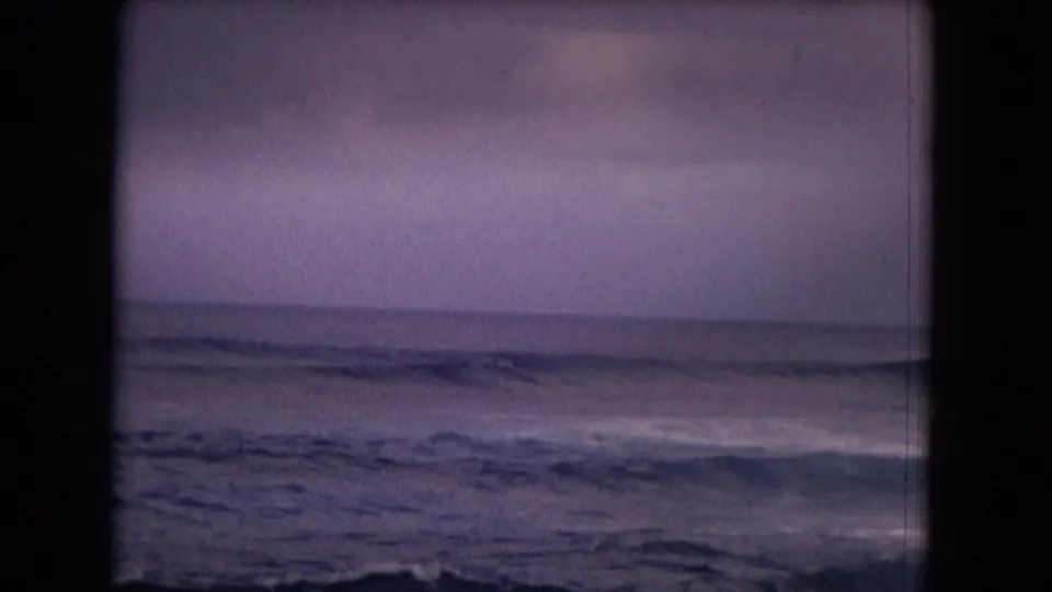 1968 Honolulu surf footage with low waves crossing the frame and a distant surfer or board shape visible offshore.