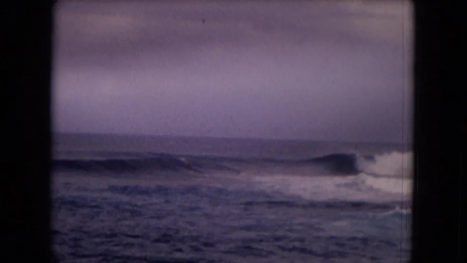 1968 Honolulu home-movie frame showing a low wave breaking across the water with soft grain and muted color.
