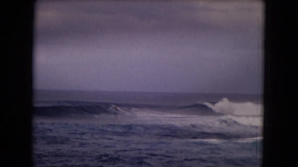 1968 Honolulu 8mm frame with white surf breaking to the right and small rolling swells under a cloudy sky.