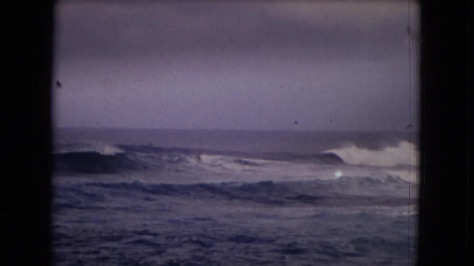 1968 Hawaii 8mm frame showing white surf rolling across a dark ocean beneath a muted, overcast sky.