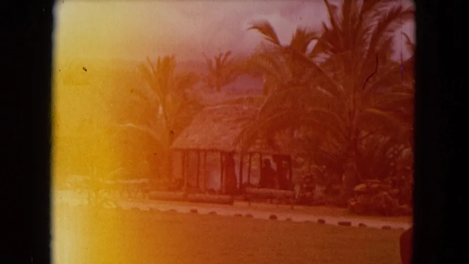 Faded 1968 Honolulu frame with a thatched hut partly obscured by orange color shift and surrounding palms.