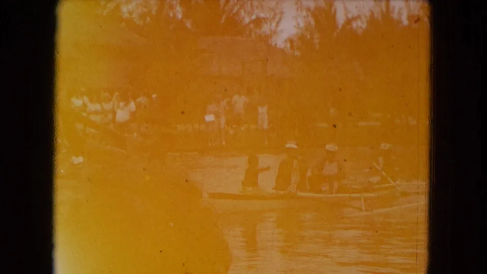 1968 Honolulu frame showing people in a small boat on the water, with palms and a thatched structure in the background.