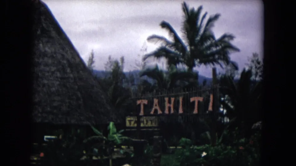 1968 Honolulu resort exterior with a prominent Tahiti sign, steep thatched roof, palm trees, dark vehicle shape, and planted grounds.