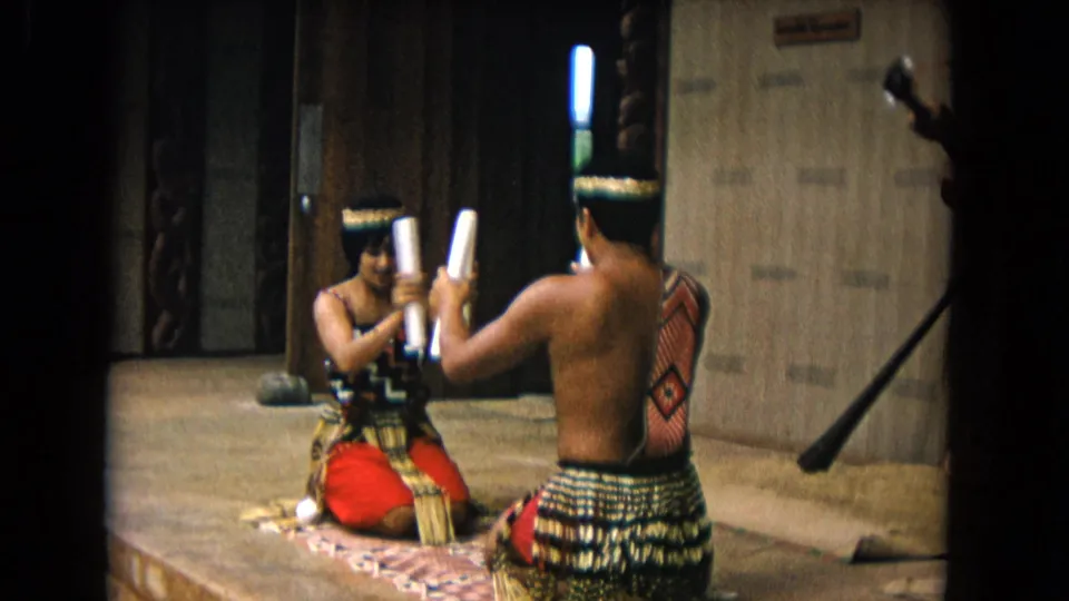 Two adult performers in Honolulu sit facing each other as their white sticks meet during a 1968 indoor cultural performance.
