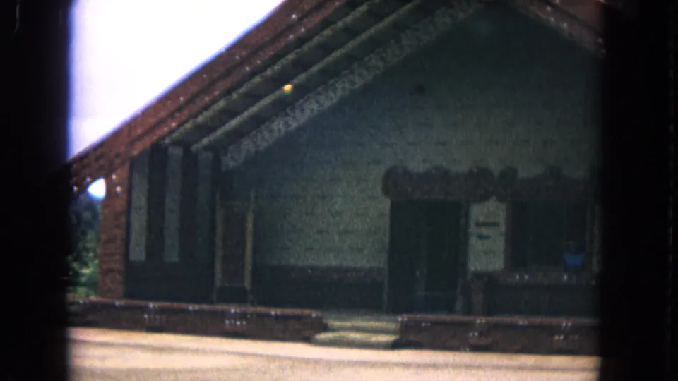 1968 Honolulu frame showing the carved meeting-house entrance and gabled roofline from a visitor's handheld 8mm perspective.