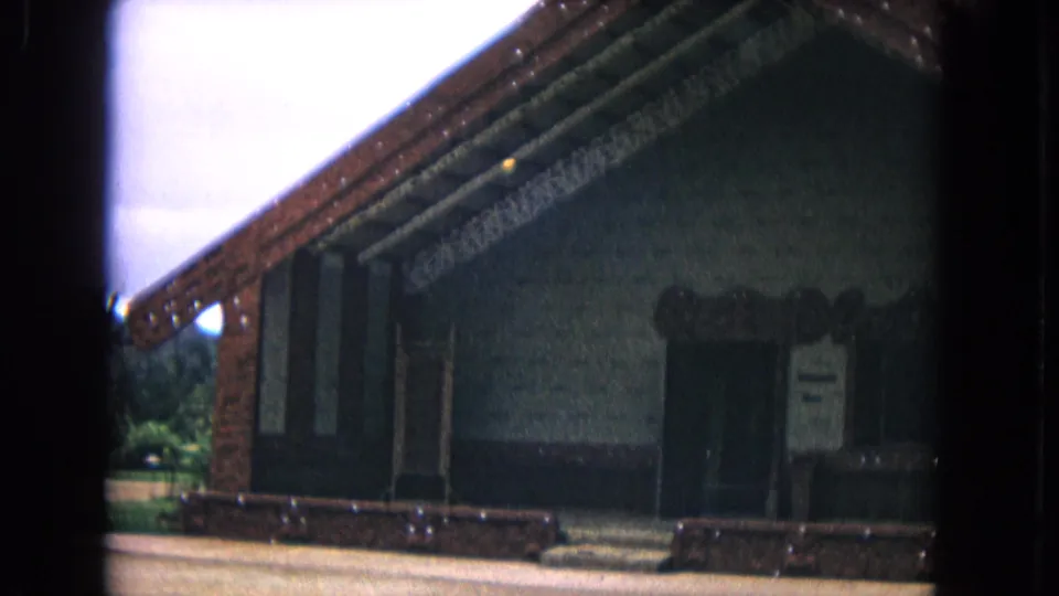 1968 Honolulu 8mm frame showing a low-angle view of a dark, steep-gabled structure with carved trim and a shaded doorway.
