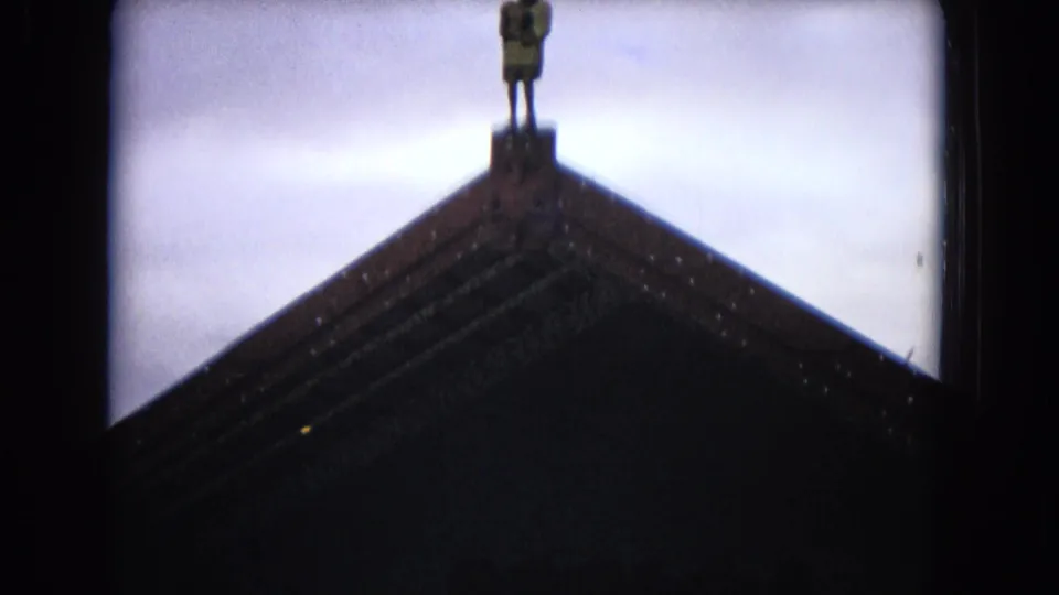 1968 Honolulu 8mm frame showing a small standing figure silhouetted on the peak of a steep gabled roof against the sky.
