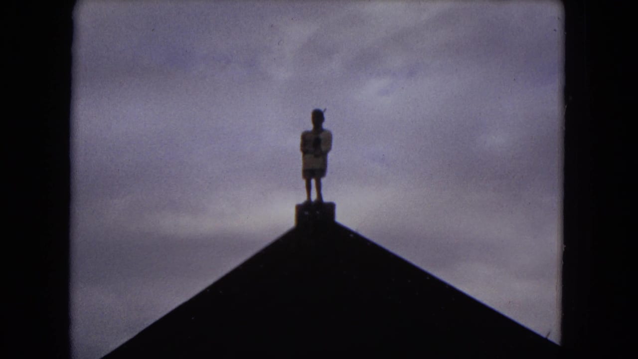 1968 Honolulu 8mm frame showing a small figure or statue silhouetted on a peaked roofline beneath a muted sky.