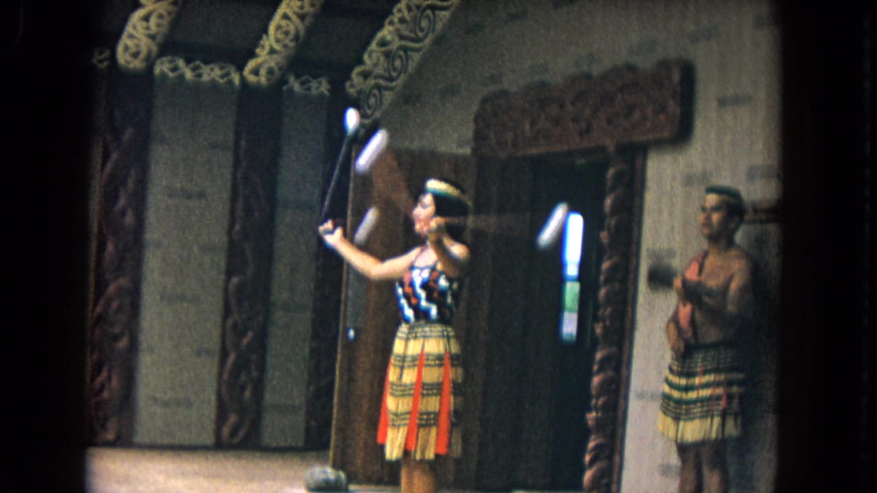 Female performer holds juggling clubs near a male performer inside a carved wooden structure.