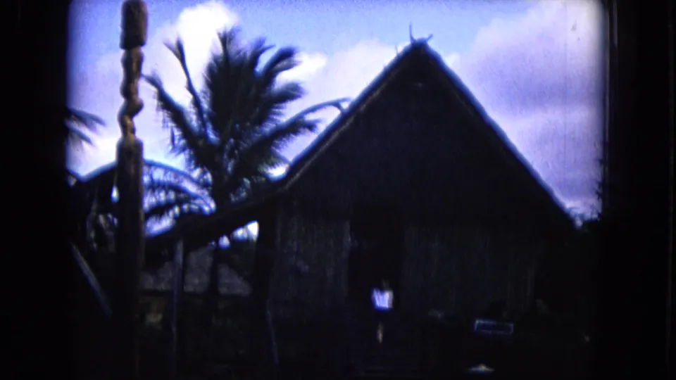 1968 Honolulu 8mm frame showing a dark thatched-roof hut with palm trees and heavy shadow around the frame edges.