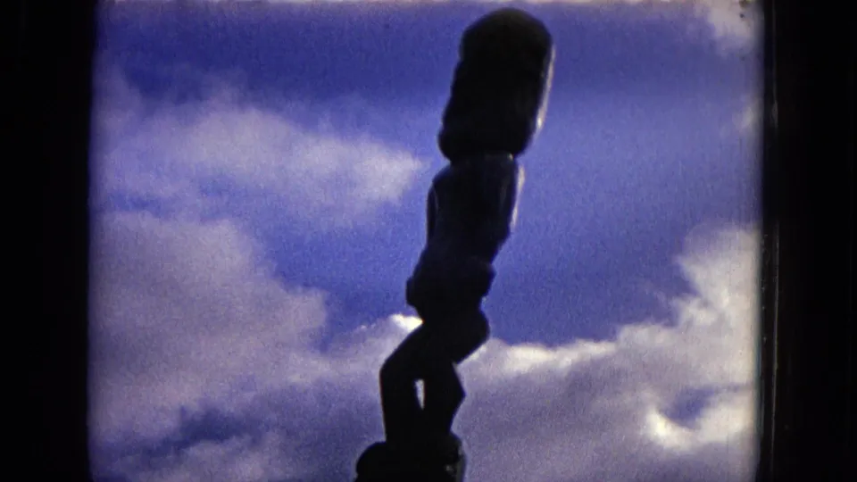 1968 Honolulu 8mm view of a tiki-style statue silhouetted against bright clouds and blue sky.