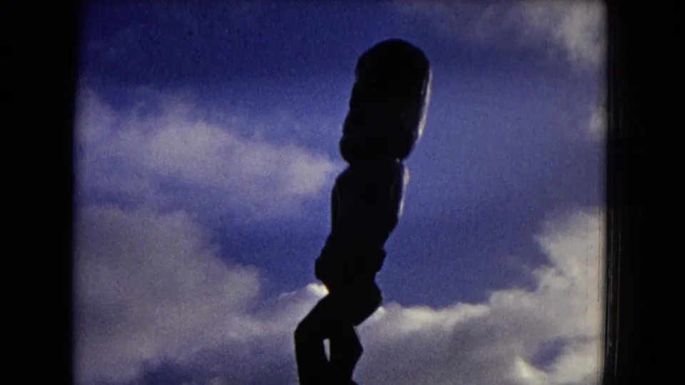 1968 Honolulu 8mm frame with a dark tiki-style statue profile set against a blue, cloud-filled sky.