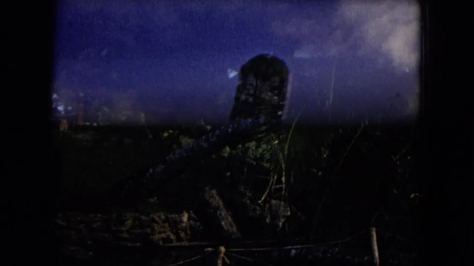 1968 Honolulu 8mm frame showing dark tropical vegetation and a partially visible tiki-style statue beneath clouds.