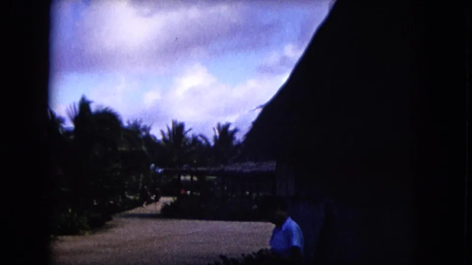 1968 Honolulu travel frame with thatched roofs, a path, palms, sky, and a distant person in a light blue shirt.