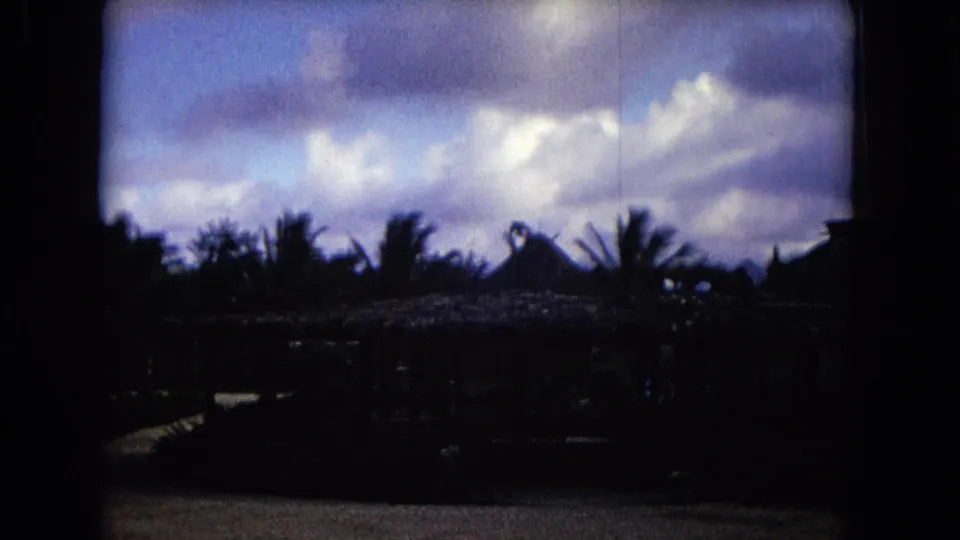Shadowed Honolulu resort-like structures and palms sit beneath a bright, clouded sky in a 1968 8mm frame.