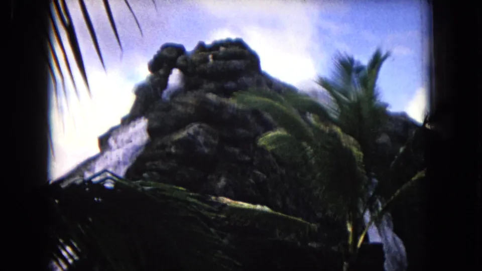 1968 Honolulu travel frame showing a rocky outcrop, palm fronds, and a waterfall with heavy 8mm shadowing at the edges.