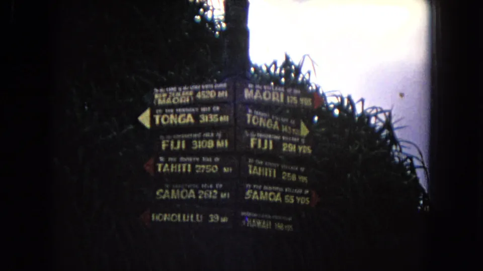 1968 Honolulu 8mm frame with a dark, high-contrast close-up of a signpost pointing toward Pacific islands including Tonga, Fiji, Tahiti, and Samoa.