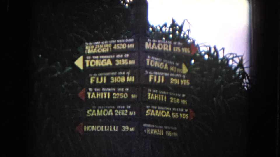 1968 Honolulu frame showing stacked directional signs for Pacific destinations, filmed through saturated 8mm color.