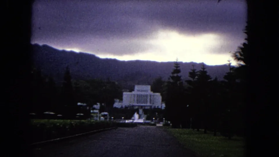 In this 1968 Hawaii home-movie frame, the white temple-like building appears larger as the driveway, lawns, trees, and dark hills fill the view.