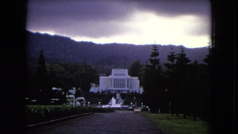 Final 1968 Hawaii frame with the white temple-like landmark centered beyond the drive, surrounded by tropical greenery, hills, and a luminous storm sky.