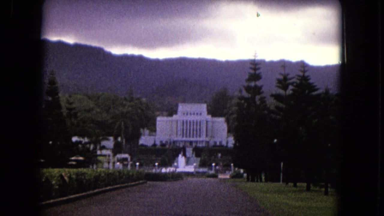 White memorial-like building beyond a lawn and road, with trees and mountains in the background.