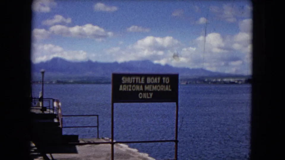 1968 Honolulu waterfront frame with a readable Shuttle Boat To Arizona Memorial Only sign, pier railings, harbor water, and mountains.