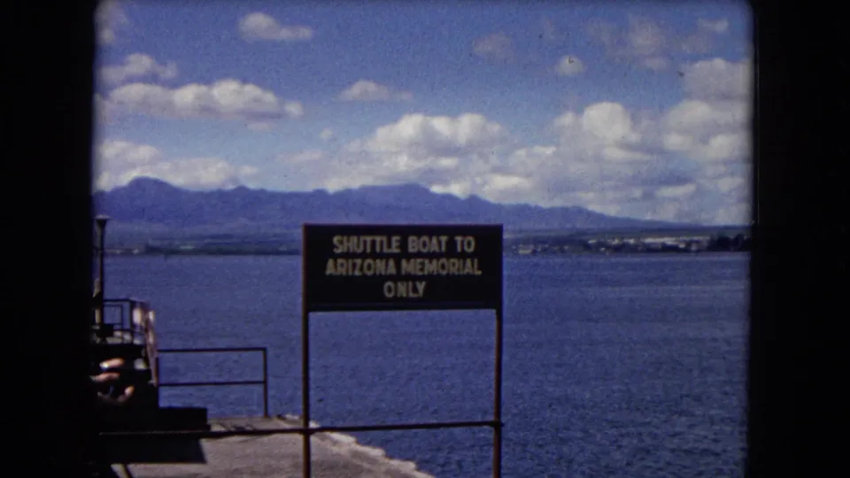 1968 Honolulu frame showing the Shuttle Boat To Arizona Memorial Only sign at the waterfront, backed by blue harbor water and mountains.