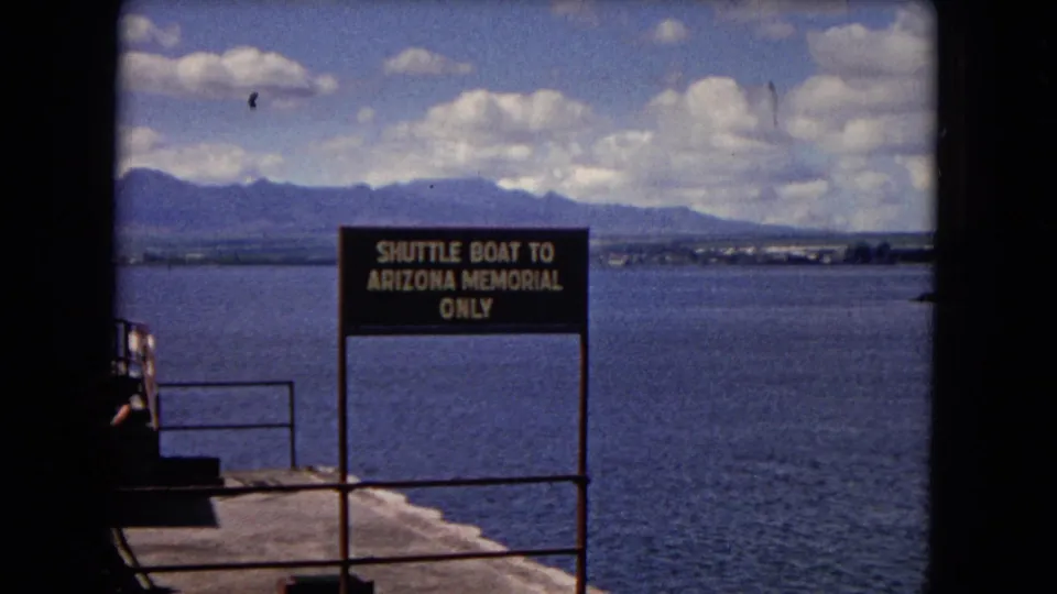 1968 Honolulu 8mm frame of the Arizona Memorial shuttle boat sign with calm harbor water and distant mountains under clouds.
