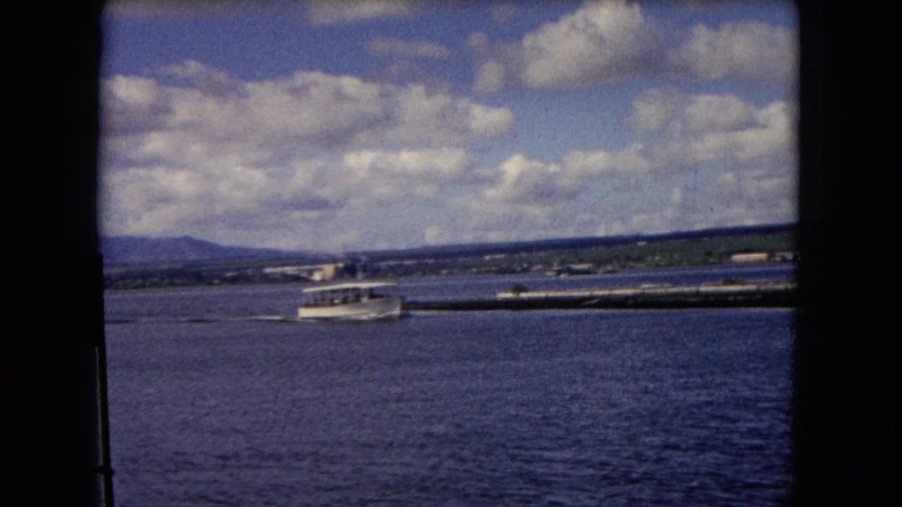 1968 Honolulu harbor view with a small white shuttle boat moving across blue water under a partly cloudy sky.