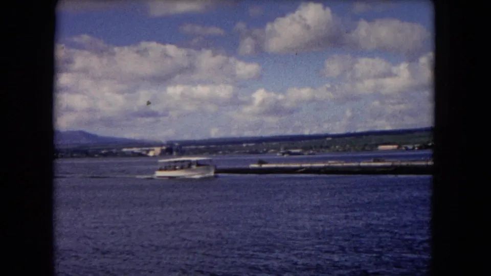 Small white boat on Honolulu waters, seen through dark 8mm frame borders with distant land and clouds.