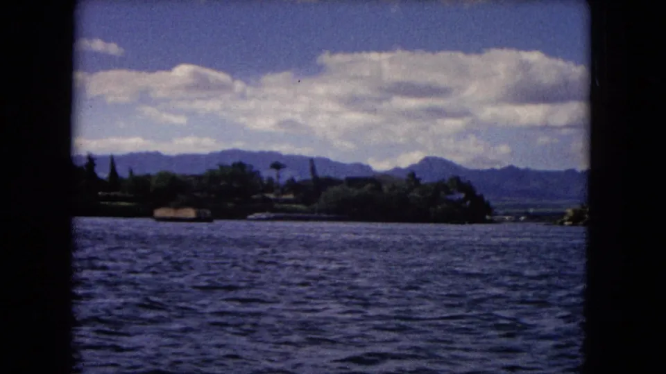 Honolulu waterfront landscape with rippled water, dark shoreline trees, and mountains beneath a broad cloud bank.