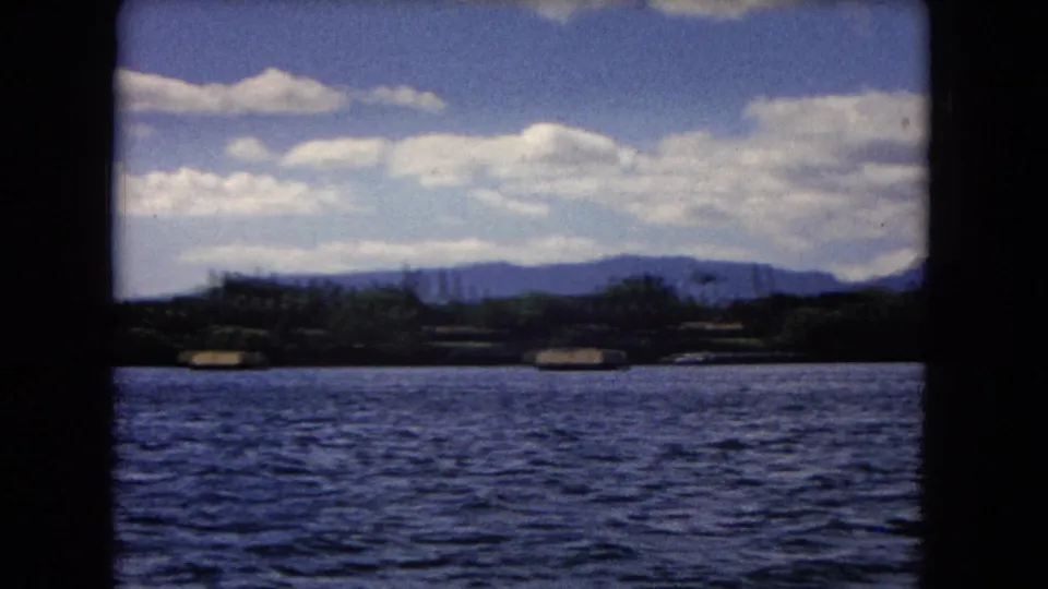 Wide 1968 Honolulu water view with shoreline vegetation and low mountains framed by dark 8mm borders.