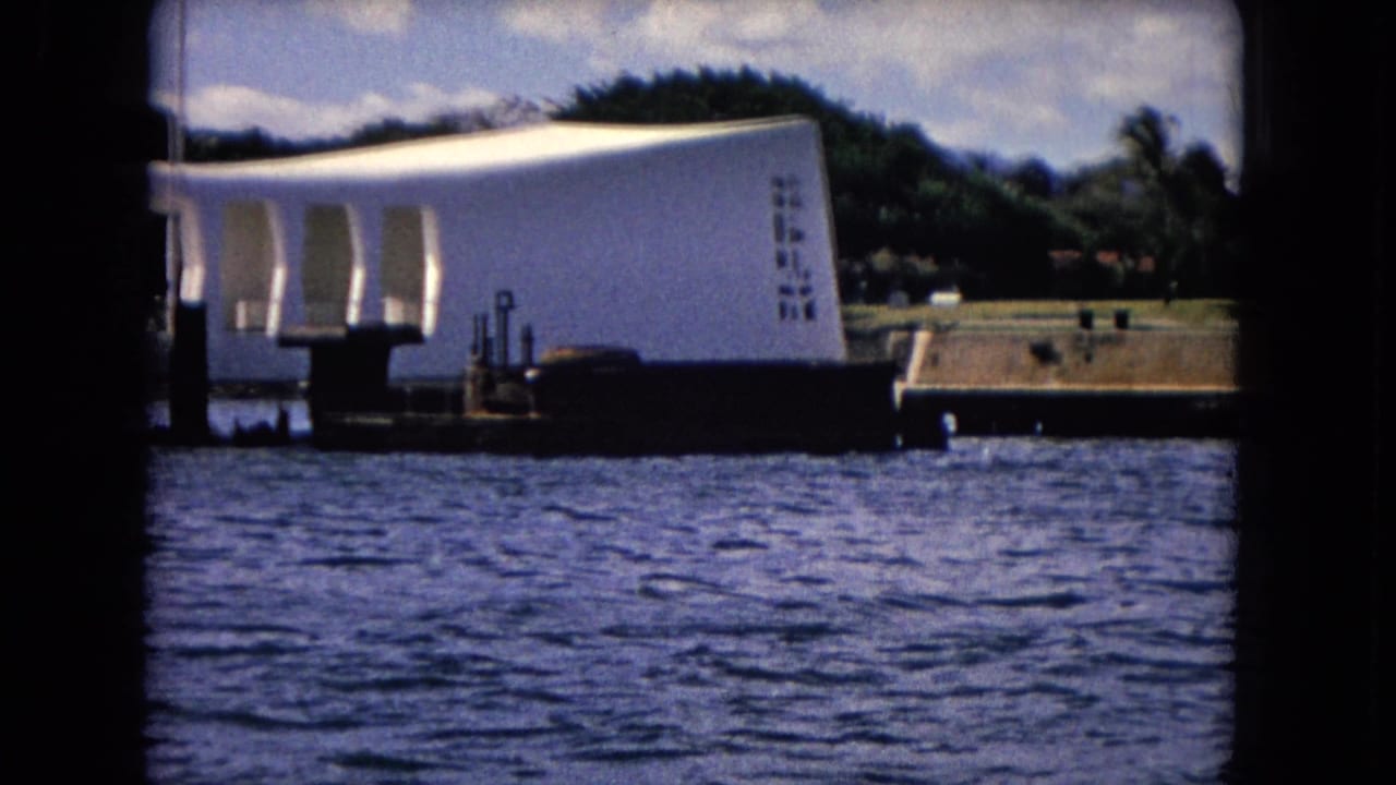 1968 8mm view of the USS Arizona Memorial at Pearl Harbor, with white arches, dark water, dock posts, and shoreline trees.