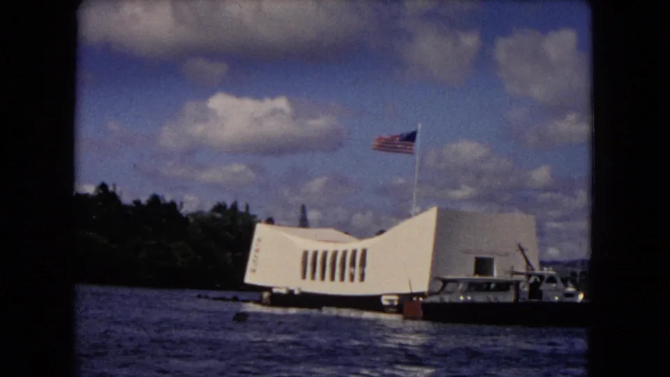 1968 Pearl Harbor view of the white USS Arizona Memorial, American flag, tour boat, water, and tree-lined shore.