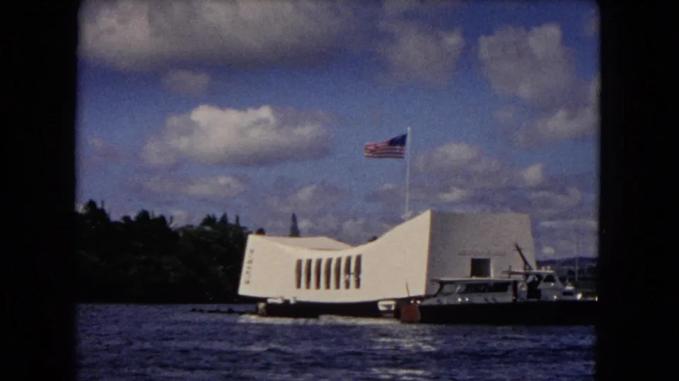 Visitor-shot 1968 Honolulu frame with the USS Arizona Memorial, American flag, nearby boat, harbor water, and shoreline trees.