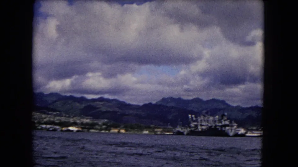 1968 8mm frame showing ships near the Honolulu coast, with mountains and heavy clouds in the distance.