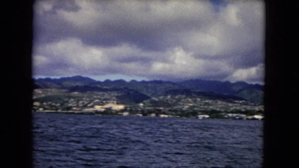 Honolulu coast and mountain ridge remain visible across blue water under thick clouds in this 1968 home-movie frame.
