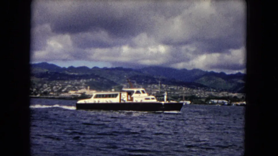 A white and dark motorboat crosses the choppy Honolulu harbor water, leaving a wake below the mountain skyline.