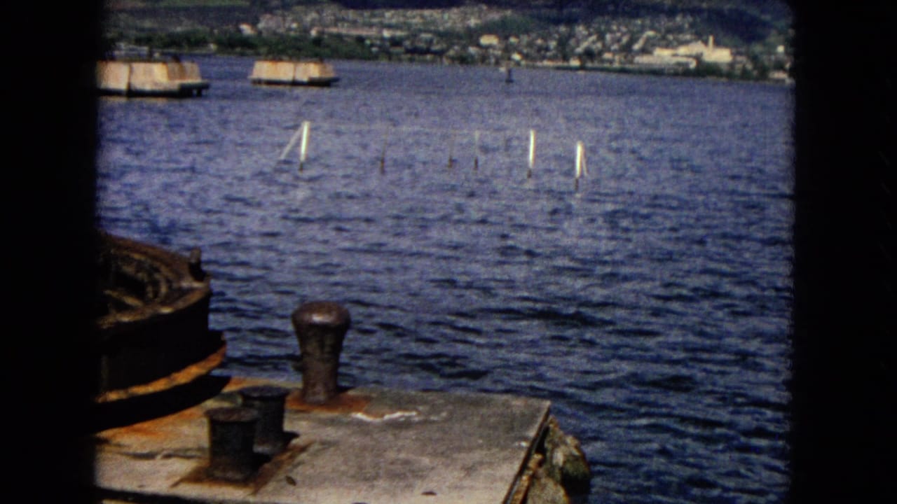 1968 Honolulu harbor view showing rusted deck hardware, blue water, small boats, and a distant shoreline in 8mm home-movie framing.