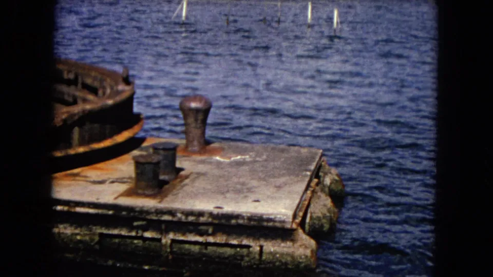 1968 Honolulu harbor footage frames a corroded metal edge and deck fittings against blue water, with no people or readable markings visible.