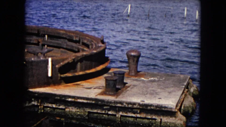 The 8mm frame shows a weathered circular metal structure, rust-stained deck surface, bollards, and Honolulu harbor water in the background.