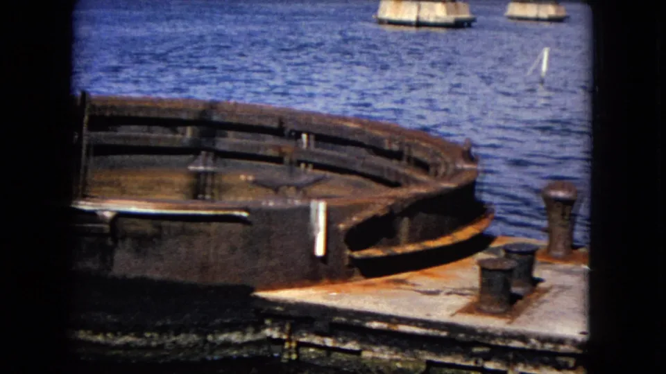 1968 Honolulu harbor view with a rusted round vessel edge, deck hardware, blue water, small boats, and dark 8mm frame borders.